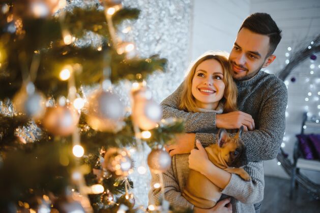 女人圣诞节前夕 一对年轻漂亮的夫妇在喜庆的新年客厅里和他们的狗玩耍年轻快乐拥抱