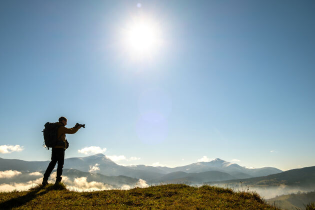 调整背包摄影师用数码相机拍摄秋山晨景的剪影自然日出剪影