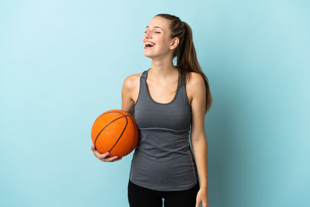 爱好年轻女子打篮球孤立在蓝色背景笑在横向位置运动员微笑大笑