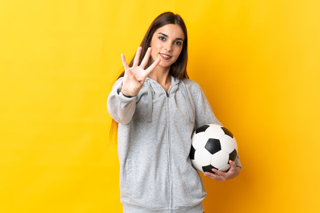 比赛年轻的足球运动员 一个被隔离在黄色背景下的女人 快乐地用手指数着四个四女孩女子