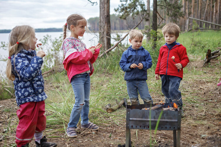 吐司一群孩子坐在火炉旁 准备在营火上烤棉花糖糖 周末徒步旅行 在当地禁闭后旅行 留宿女儿一起公园