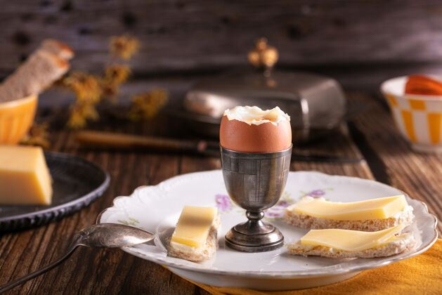 面包木桌上放着煮鸡蛋的银蛋杯 还有面包和奶酪蛋黄黄油自然