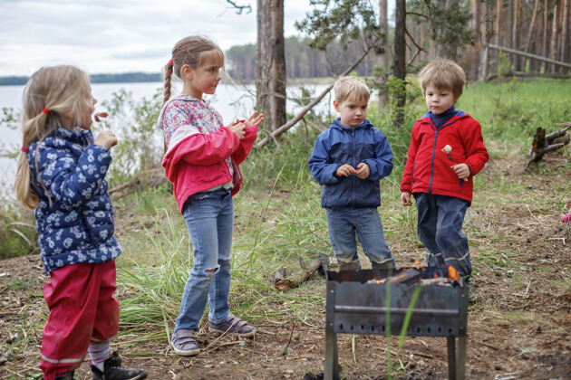 吐司一群孩子坐在火炉旁 准备在营火上烤棉花糖糖 周末徒步旅行 在当地禁闭后旅行 留宿女儿一起公园