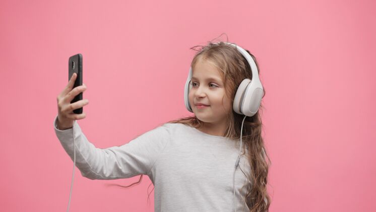 快乐快乐的孩子戴着耳机在智能手机的移动应用程序中选择最喜欢的音乐曲目童年年轻女孩