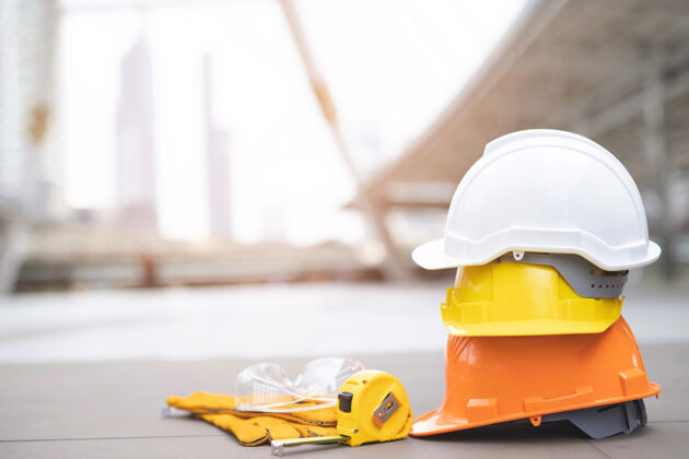 混凝土橙色 黄色 蓝色和白色的安全帽在工程施工现场戴在水泥地面上的建筑物上安全帽安全项目