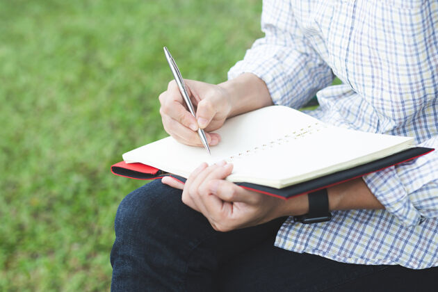 笔记本年轻人手里拿着用蓝色铅笔打开的笔记本 放在带书签的木质桌子上教育女性写作