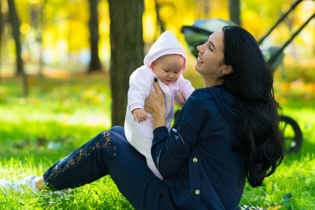 阳光秋天 快乐的年轻妈妈和一个可爱的女婴在公园的草地上玩耍秋天抚养一起