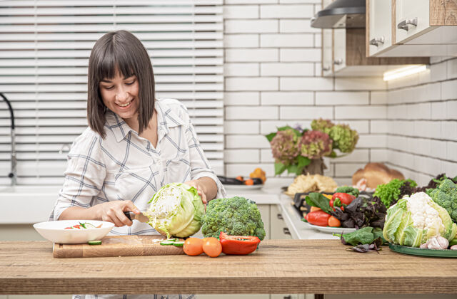 健康漂亮的黑发女人微笑着在现代厨房的室内空间里切卷心菜做沙拉饮食维生素蔬菜