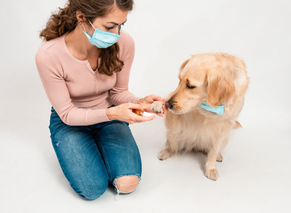 保健戴着医用防护面罩的女孩用消毒剂给狗的爪子消毒冠状病毒保护女人