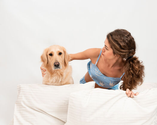 床快乐的女性穿着睡衣和她的金毛猎犬一起睡在床上动物一起肖像