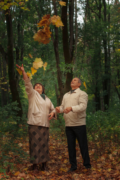 欢呼一对领养老金的夫妇在秋天的公园里散步 抛起黄叶户外秋天女人