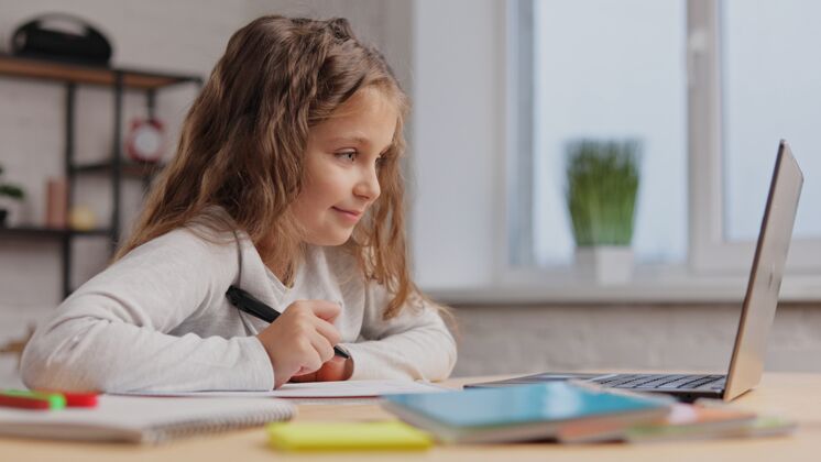 冠状病毒可爱的小学生在家用笔记本电脑学习电脑女学生有网络课 写练习本 做作业女孩课隔离