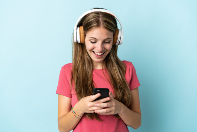 音乐年轻的白种女人 孤独地站在蓝色的背景下 一边听音乐 一边看手机歌曲聆听成人