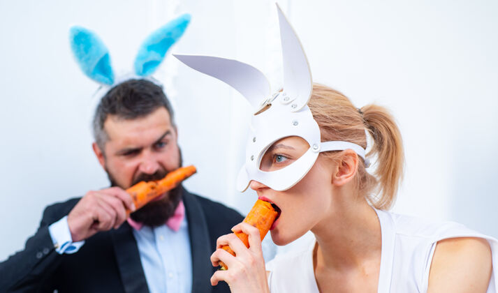 大胡子男人有趣的家庭庆祝复活节复活节兔子兔子一对快乐假日情侣用兔子耳朵吃胡萝卜复活节画笔女人