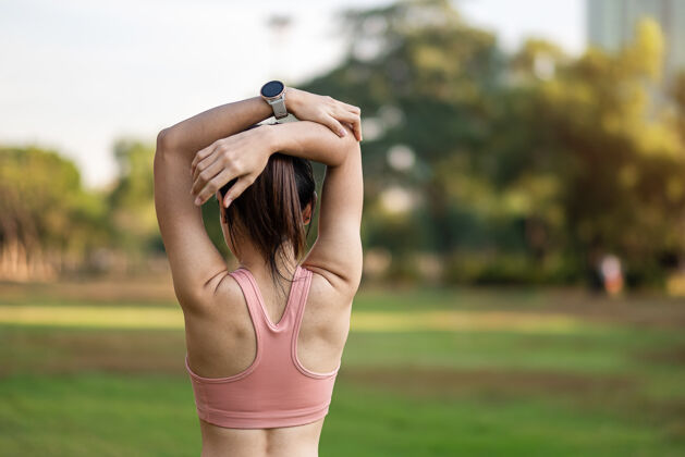 工作穿着粉色运动服的年轻成年女性在公园户外伸展肌肉 运动女性热身准备跑步和慢跑早上好健康 健身 运动和工作生活平衡概念锻炼肌肉身体
