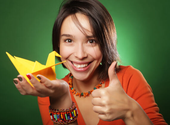 折纸一个年轻的表情女人 在绿色的墙壁上带着纸鸟成人漂亮看起来