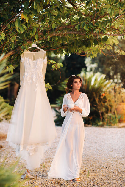 意大利婚礼一位美丽的新娘站在一件婚纱旁边 端着一杯茶 身着闺房装 旁边是一座别墅意大利早上好托斯卡纳的新娘华丽豪华优雅