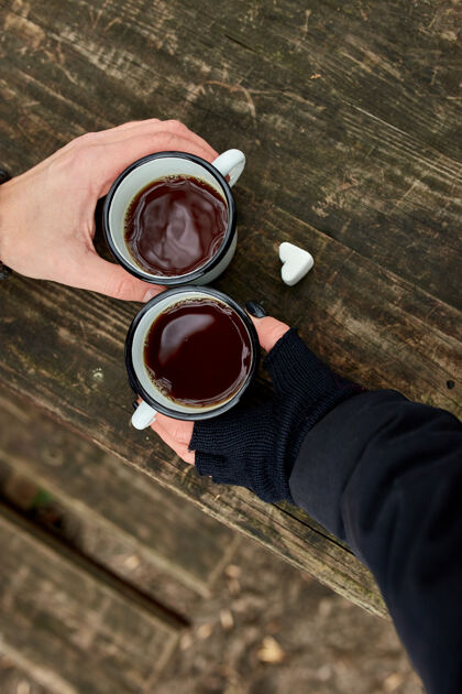 休闲两杯茶在大自然中的情侣手中 戴着黑手套放在木头表面感觉风景放松