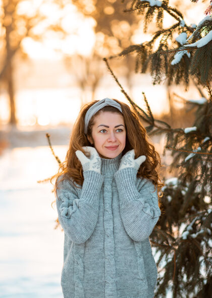 冬装冬天的肖像画 年轻漂亮的卷发黑发女子穿着灰色针织毛衣覆盖在雪上姿势成人季节