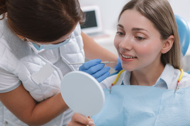 牙科可爱的年轻女子在牙医的牙科治疗中照镜子职业牙科保健