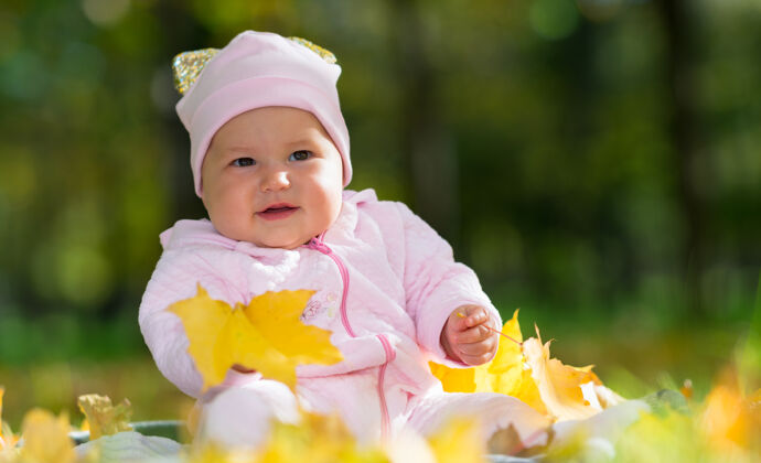 秋天一个穿着粉红色衣服的好奇的婴儿在黄色的秋天玩耍 秋天的树叶在公园里的景色地毯年轻健康