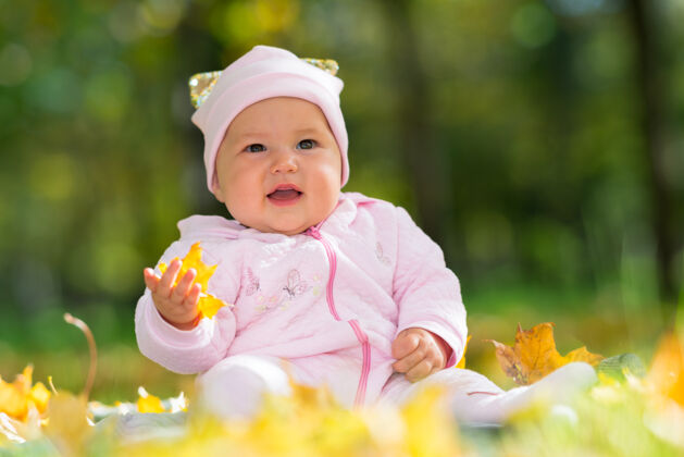 人在秋天的公园里 穿着粉色衣服的可爱小女婴在树林的映衬下 低角度地玩着五颜六色的黄叶花园地毯独自
