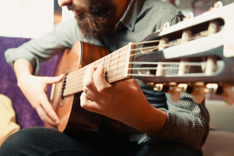 人在一个明亮的日子里 一个留着胡子的男奏西班牙吉他的手的特写镜头男性现代时髦