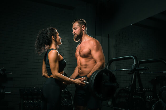 举重侧视图迷人的女性帮助肌肉发达的男性举起沉重的杠铃 而在现代健身房一起工作帮助健康活力