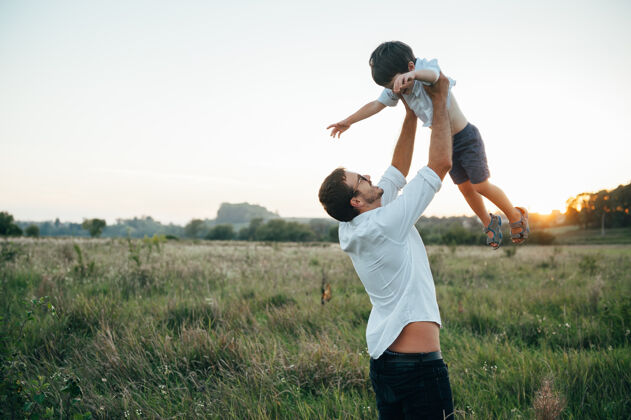 家庭英俊的爸爸带着他可爱的小儿子在绿草如茵的草地上玩耍父亲快乐享受