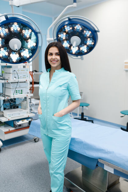 礼服微笑的女外科医生在手术台前摆姿势 背景灯亮着职业卫生擦洗