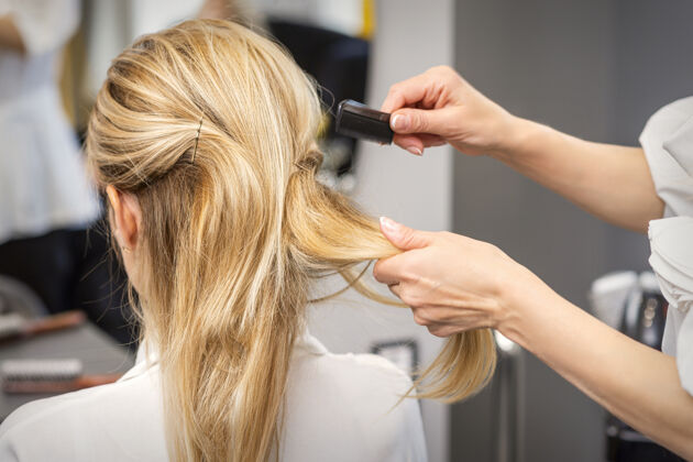 成人一个美发师的后视图梳头金发的年轻女子在美容院新娘发型沙龙