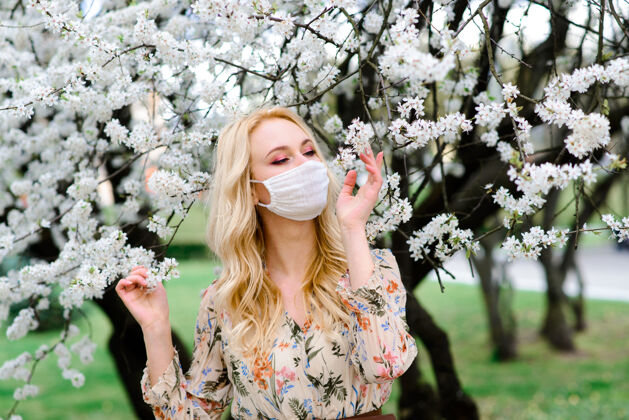 呼吸器在春天的花园里 一个戴着无菌医用防护口罩的年轻女子污染花朵户外