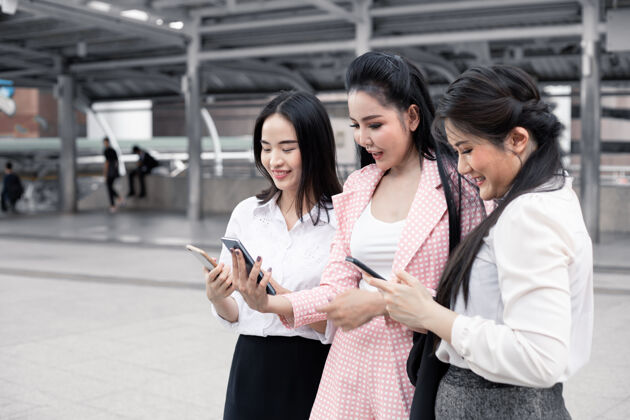 进步一群在户外微笑着玩手机的亚洲女商人城市概念亚洲团队精神女士.泰语女上班族移动人员员工