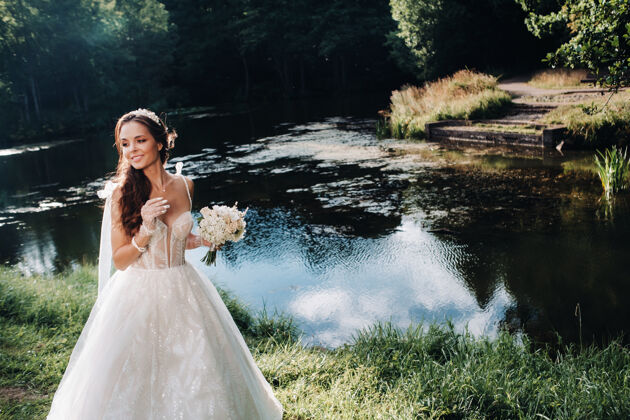 女人一个优雅的新娘在一个自然公园里穿着白色的裙子和一束花束的肖像自由微笑户外
