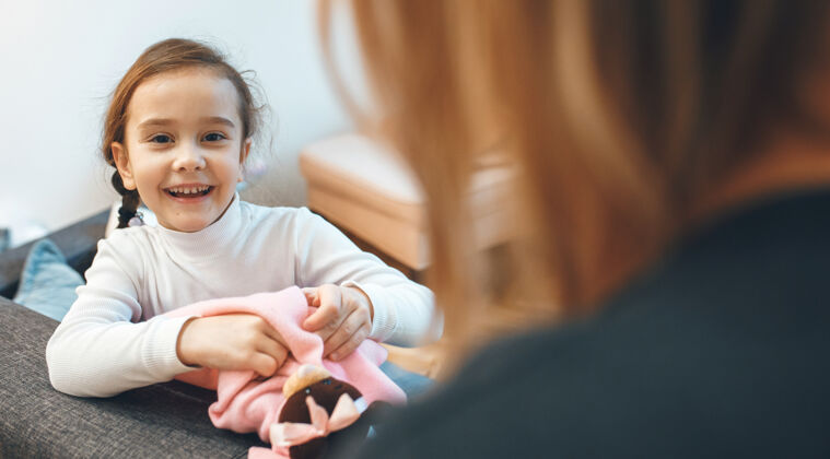 女孩快乐的女孩和她的妈妈在客厅里玩泰迪熊沙发软玩具表达