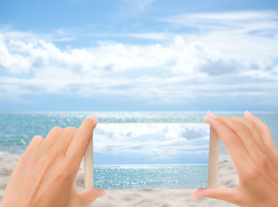 海洋手拿手机的女人在蓝色的海洋和蓝色的天空模糊的图像上看海放松自然海洋