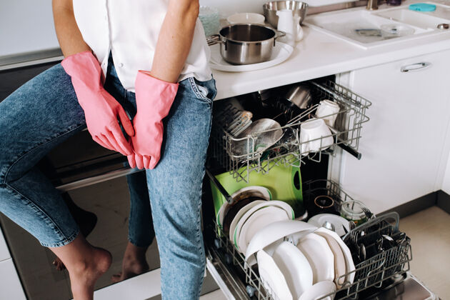 室内一个戴着粉红色手套的家庭主妇女孩在打扫完房子后累得坐在屋里厨房.in白色的厨房里 女孩洗过盘子 正在吃饭休息很多洗过的盘子消毒卫生餐具