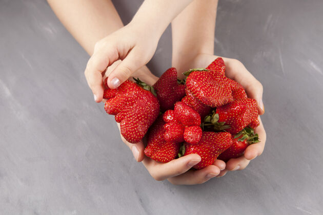 奇怪概念-吃难看的水果和蔬菜.儿童她的手拿了一个成熟的奇怪形状的草莓从女性手灰色背景 复制空间生动潮流缺陷