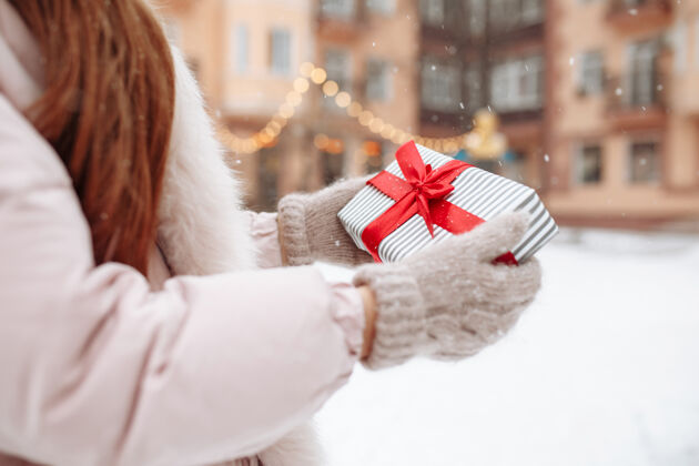 快乐特写镜头白色礼品盒与红色丝带在一个女人的手上穿着温暖的羊毛手套在外面的冬天下雪瓦伦丁公园情人节 圣诞节和冬天女朋友礼物约会