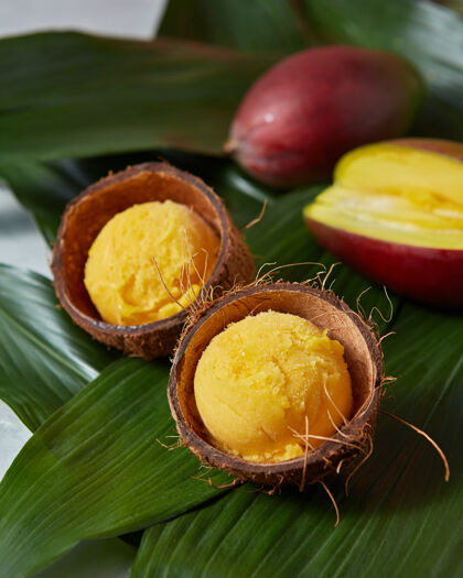 芒果新鲜可口的黄色水果冰淇淋椰子皮和半新鲜芒果绿棕榈树叶夏天概念自制碗五颜六色