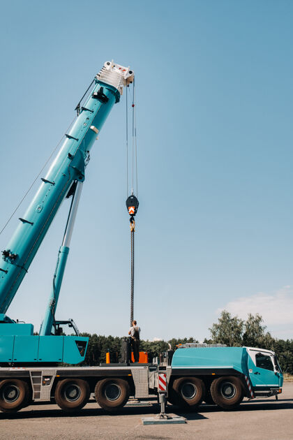 金属配重是由一个不知名的工人安装在一个大型蓝色汽车起重机上 并准备在一个大型现代化建筑旁边的工地上工作运输吊钩安装