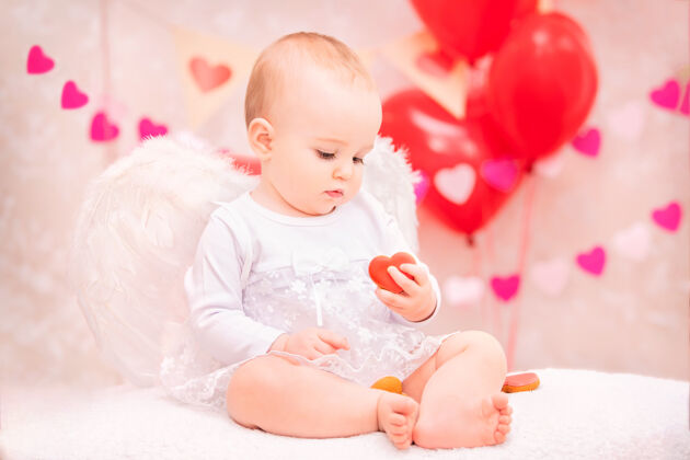 人长着白色羽毛翅膀的婴儿吃着心形饼干 象征着情人节孩子天使女