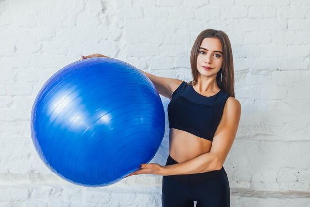 私人教练在白色健身工作室拿着蓝色健身球的快乐女人的画像女孩运动健康