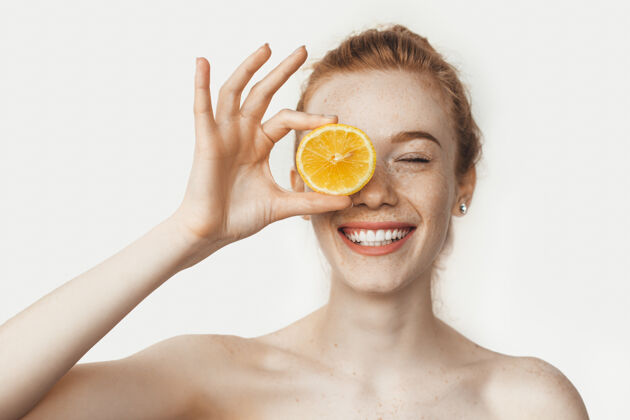 快乐光着肩膀 满脸雀斑 满脸笑容的女人在白色的墙上摆着柠檬色的姿势成人情绪健康饮食