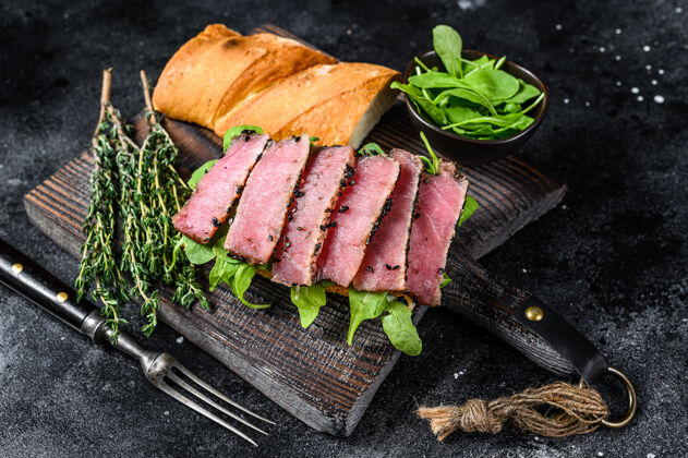 肉切菜板上有芝麻菜的法式金枪鱼牛排三明治砧板晚餐面包