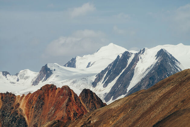 雪帽极简主义美丽的阿尔卑斯山景观 巨大的雪山在鲜明的红色峭壁后面风景冰川阳光