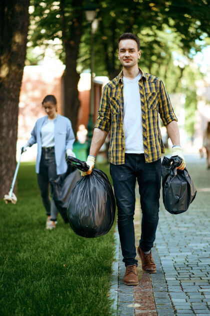 志愿者年轻人在公园里拿着塑料垃圾袋 志愿服务男人清林 生态修复 生态生活方式 垃圾回收利用 生态关爱 环境清洁友谊慈善垃圾