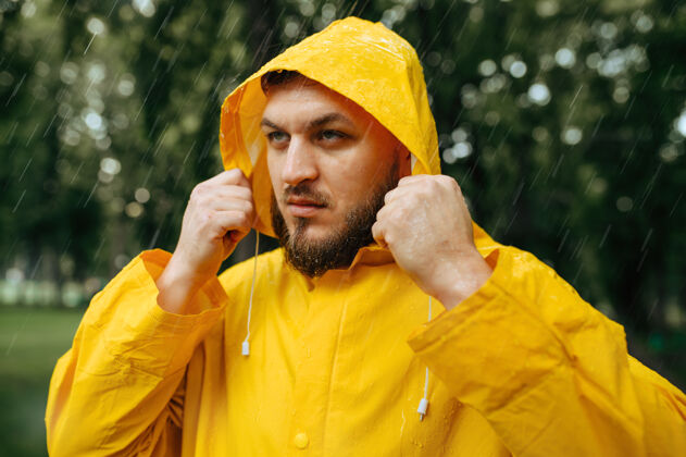 孤独穿雨衣的人戴上风帽 夏天公园里下雨一天一个人男人穿着雨衣走在小路上 小巷里天气潮湿白天冒险户外
