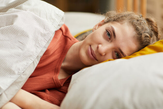 微笑一幅年轻女子躺在枕头上 在家里的床上休息时注视前方的画像室内欢呼看