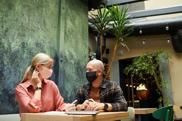 欢呼商务会议期间 商务伙伴戴着防护面具坐在咖啡厅的桌子旁沟通聚会室内